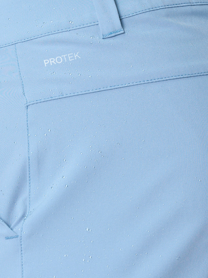 Close up of light blue golf shorts fabric with water droplets, belt loop and ProTek branding on the pocket