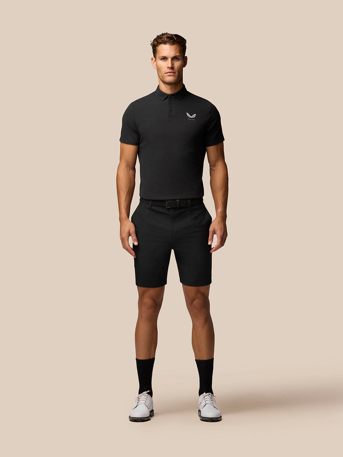 Front view of a man wearing a black Golf Club Essential Polo with Castore branding on the chest, paired with black shorts.