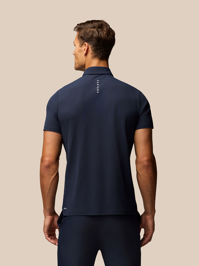 Back view of male model in navy Golf Club Essential Polo showing vertical Castore branding along the upper back