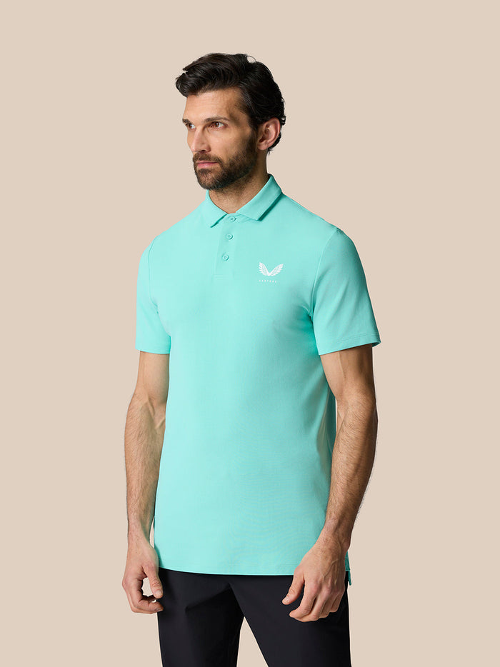 Model draagt Licht Aqua Golf Club Essential Polo met korte mouwen, puntige polokraag en Castore-logo op de borst.