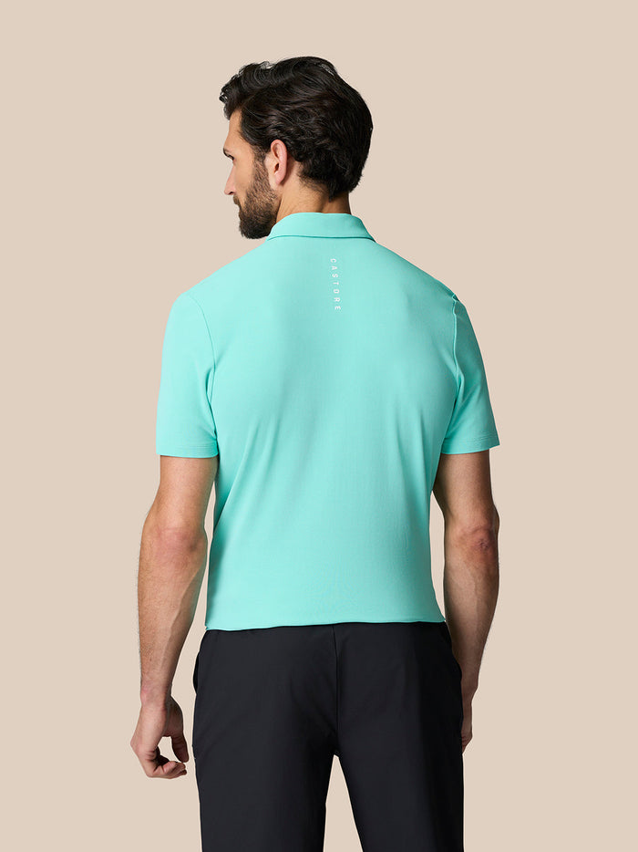 Back view of a man in a light aqua Golf Club Essential Polo showing the Castore logo along the upper back