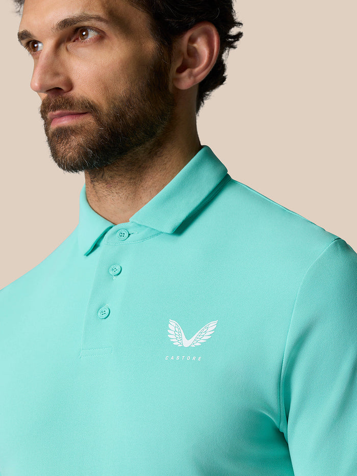 Man draagt Licht Aqua Golf Club Essential Polo frontaal gezien met kraag knopen en Castore logo op linkerborst