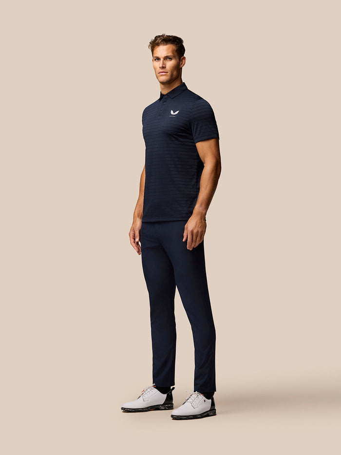Male model wearing a navy striped golf polo with three button placket and Castore logo on the chest
