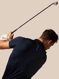 Golfer mid swing wearing navy Pinnacle Pique Stripe Polo against a beige background