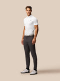 Full body of a male model in a white Golf Pinnacle Pique Gestreepte Polo with grey trousers and white golf shoes.