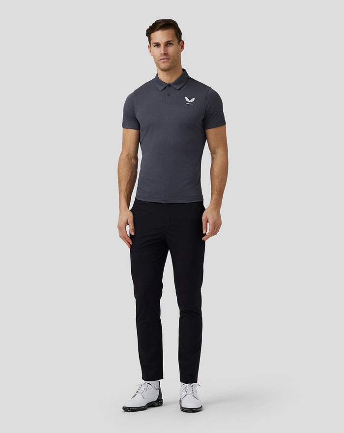 Male model wearing gray Castore Golf Pinnacle Engineered Polo with black pants and white golf shoes
