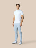 Male model wearing a white Golf Pinnacle Polo with light blue pants on a beige background