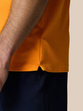 Close-up of the orange polo hem showing a side vent slit and textured knit fabric.