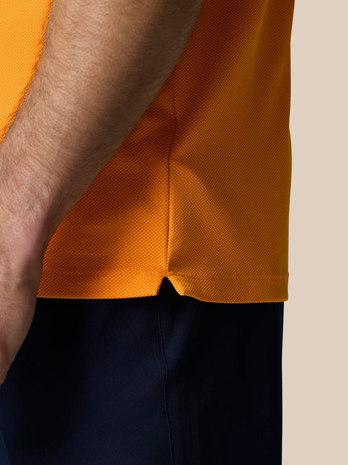 Close-up of the orange polo hem showing a side vent slit and textured knit fabric.