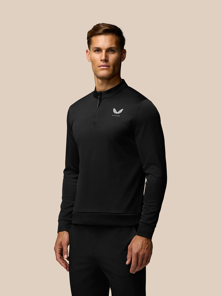 Man wearing black golf club top with quarter zip and Castore logo on the left chest