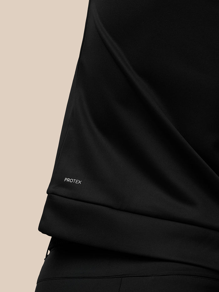 Close up of black golf top fabric with Protek branding near the hem.