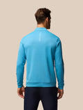 Back view of a man wearing a light blue long sleeve golf top with vertical CASTORE branding on the back.