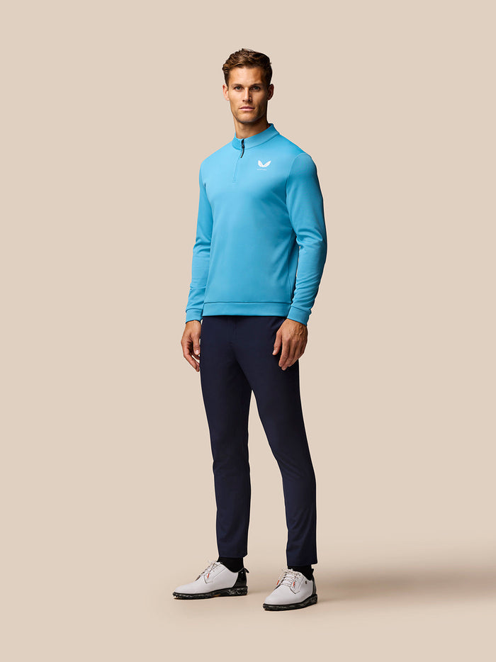 Man wearing a light blue golf long sleeve top with a quarter zip and Castore logo on the chest