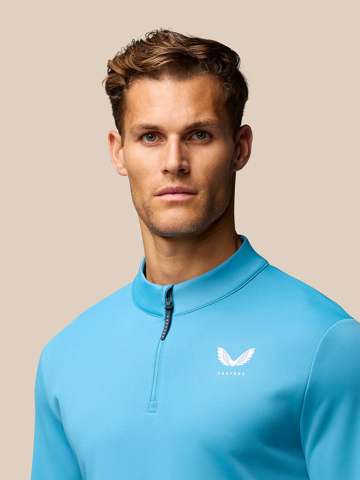 Portrait of a man in a bright blue golf top with quarter zip collar and CASTORE logo on the left chest.