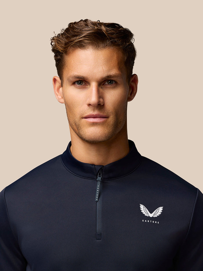 Close up of navy Golf Club Classic top showing stand collar, quarter zip and left chest Castore logo.
