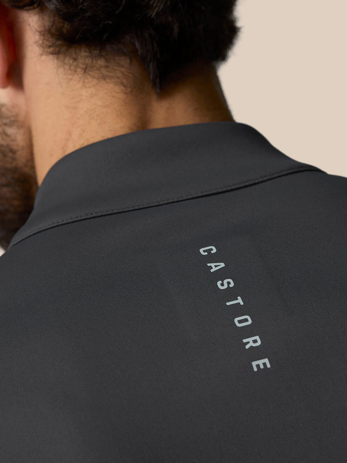 Back view of a dark golf top with a high collar and a zipper pull branded Castore