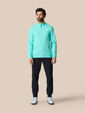 Full-body view of a man in a light aqua Castore golf top with quarter zip, dark pants, and white sneakers.