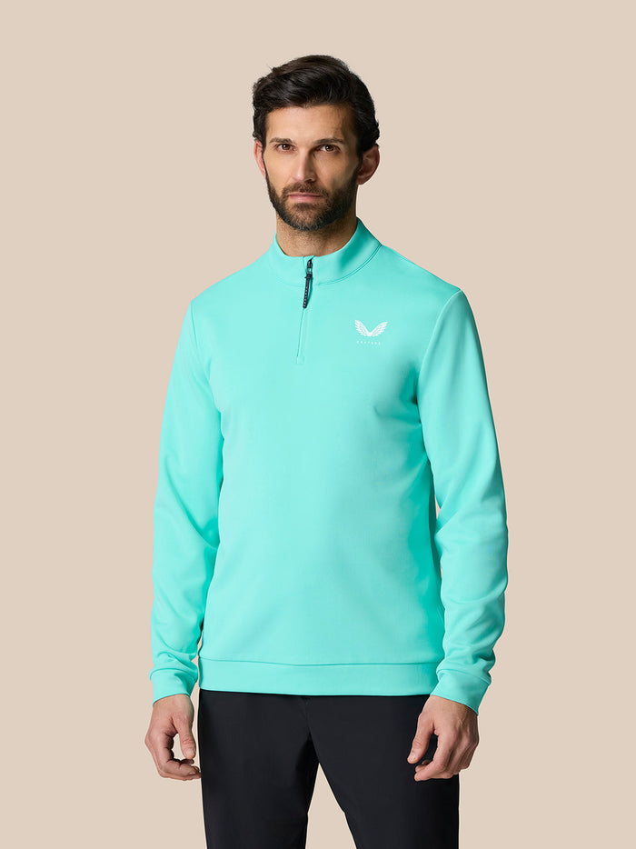 Front view of a man wearing a light aqua golf quarter zip top with a high collar and left chest Castore logo.