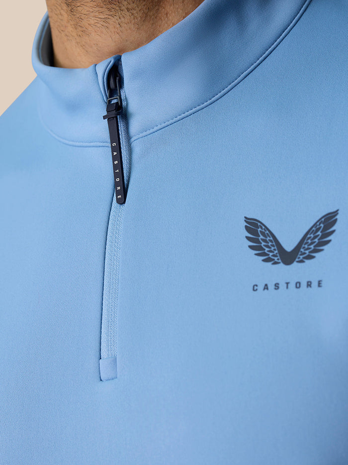 Close-up of the light blue quarter zip showing the CASTORE branded zipper pull and wing logo on the chest