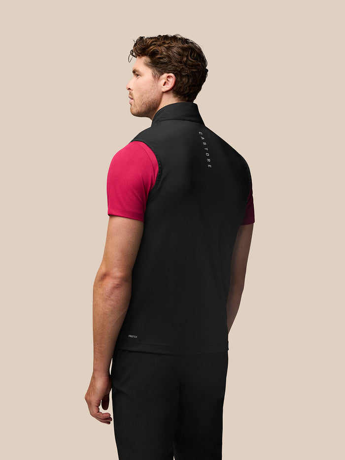 Achteraanzicht van een man in een zwarte Golf Pinnacle Gilet met roze t-shirt eronder en het Castore-logo op de kraag en bovenrug.