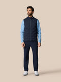 Full length view of a man wearing a navy Golf Pinnacle Gilet over a blue long sleeve top with a stand up collar