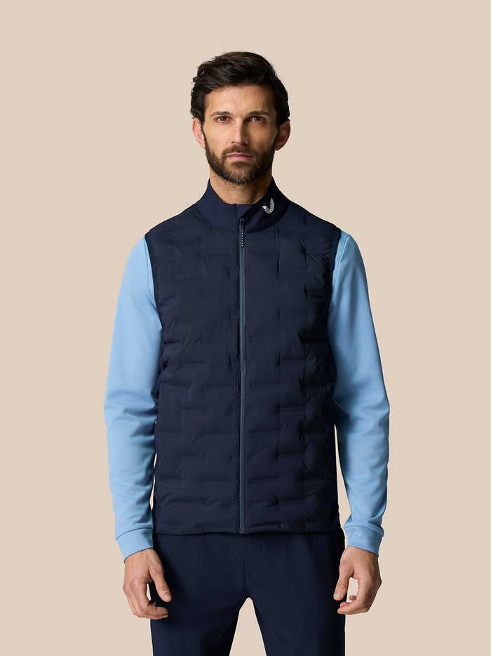 Male model wearing navy Pinnacle Lightweight Hybrid Gilet with full front zip over a light blue long sleeve top