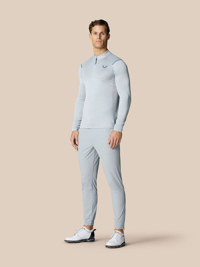 Front view of a male model in a light gray golf set with zip neck top and matching pants, white golf shoes