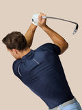 Golfer in marineblauw Pinnacle Golf Polo bereidt zich voor op een slag met de club boven het hoofd tegen een beige achtergrond