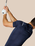 Man in marineblauw Pinnacle Golf Polo zwaait met een golfclub en witte handschoen tegen een beige achtergrond