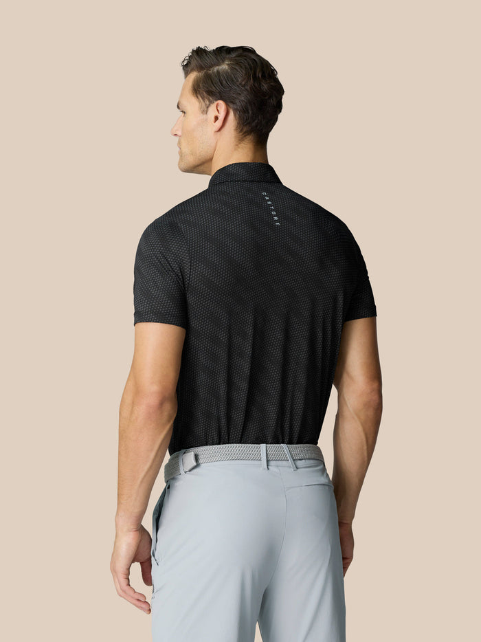 Achterkant van man in zwarte grafische polo met golfbalprint en Castore-logo langs de rug.