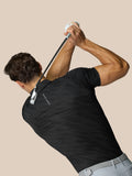 Man in zwarte grafische golfpolo met Castore-logo op borst en bovenrug tijdens een swing.