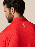Achterkant van rode polo met dot patroon en Castore logo langs de rug nabij de schouders