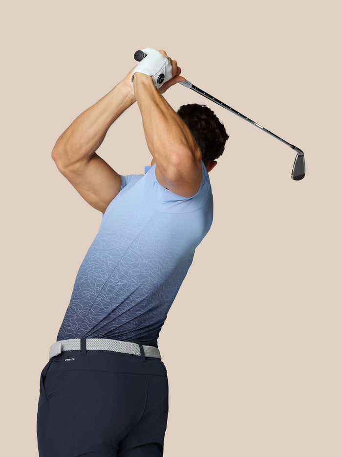 Golfer gezien vanaf de achterkant in een hemelsblauwe Club Golf polo tijdens backswing met witte handschoen en lange club.