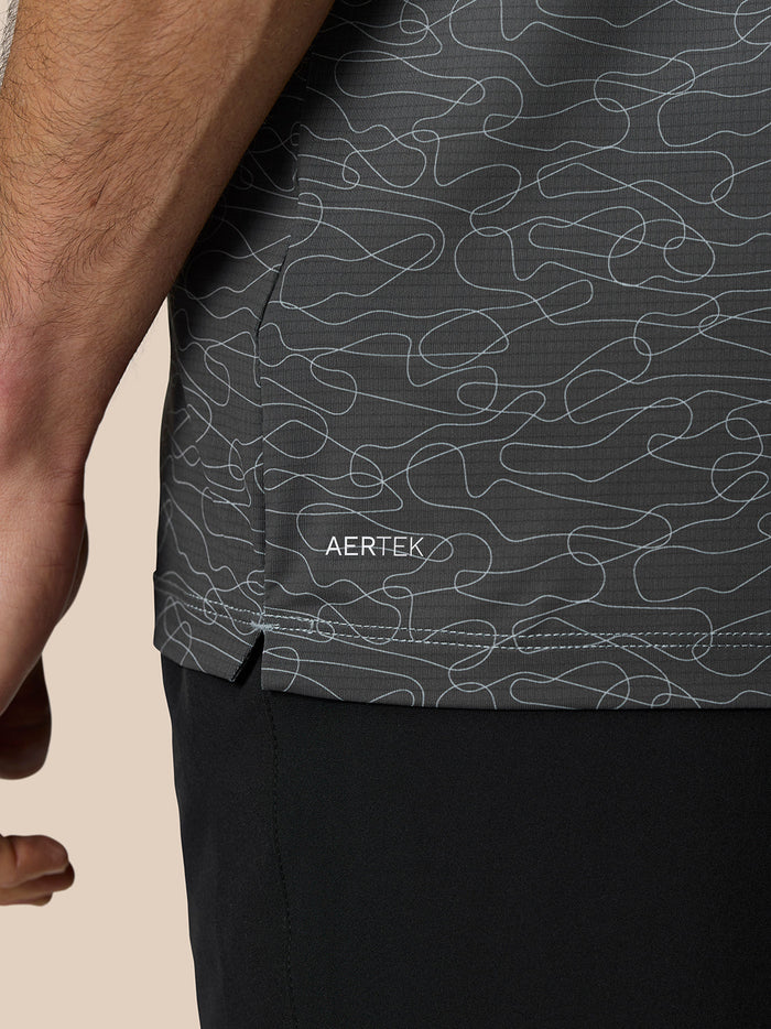 Close up of dark Club Grafische Polo fabric showing an abstract light gray squiggle print and AERTEK branding at the hem