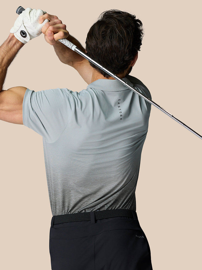 Back view of a golfer wearing a light blue Club Grafische Polo with an ombre print and CASTORE branding on the upper back