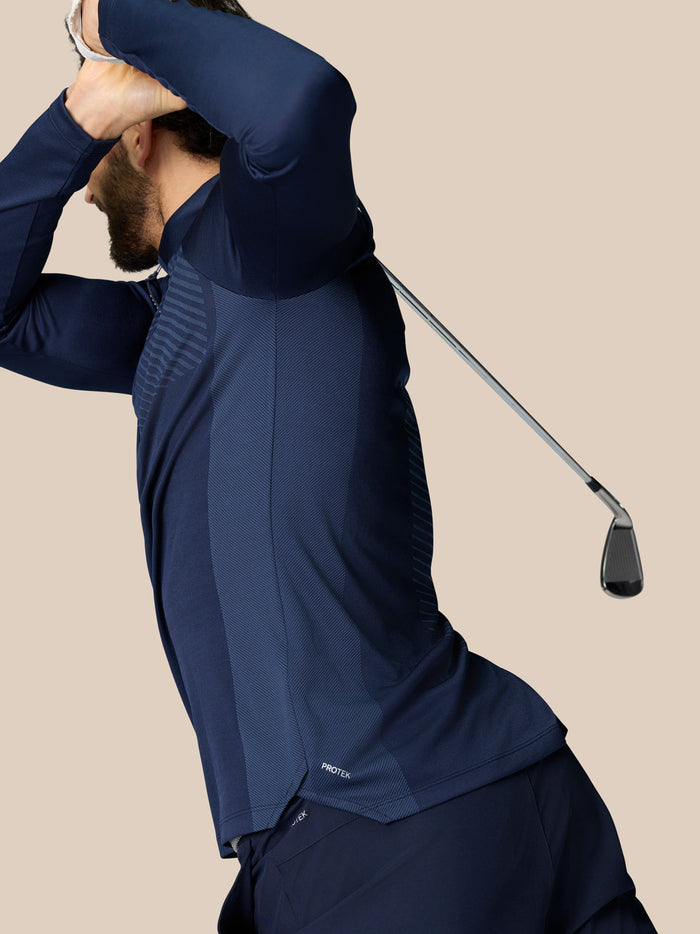 Man in navy golf quarter zip top mid swing showing ventilated panels and ProTek water resistance