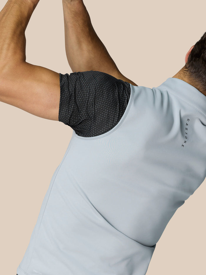 Back view of a man in a light grey sleeveless gilet with a black patterned underlayer; Castore branding on the neck and back