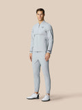 Full-body shot of a man wearing a matching light gray Golf Pinnacle woven jacket and pants with a chest logo and white golf shoes.