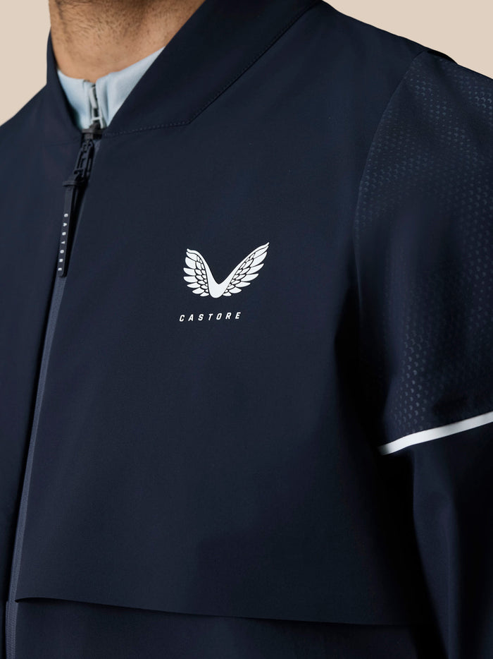 Close up of the navy Pinnacle woven jacket chest showing the white Castore wing logo and front zipper