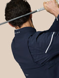 Rear view of model in navy Golf Pinnacle woven jacket with perforated sleeve panels and CASTORE collar branding while holding a golf club