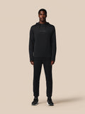 Male model wearing black Castore Flex long sleeve hoodie with hood against a beige background