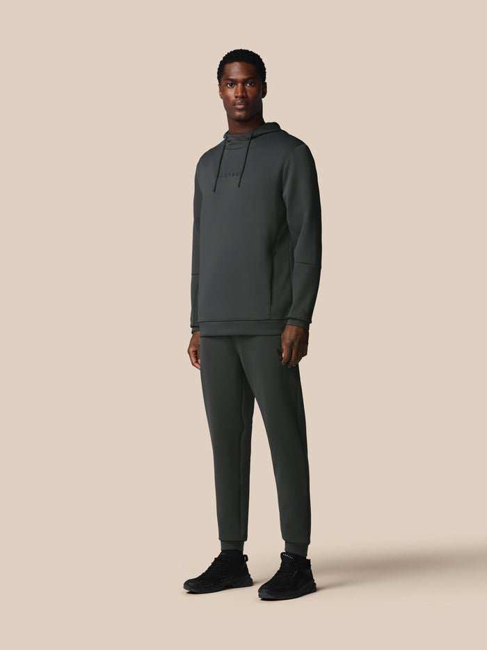 Male model wearing dark gunmetal Heren Flex Joggers with a matching hoodie and black sneakers against a neutral backdrop.