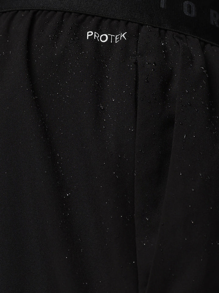 Close-up of black Adapt Training Short fabric with water droplets and ProTek branding on the waistband