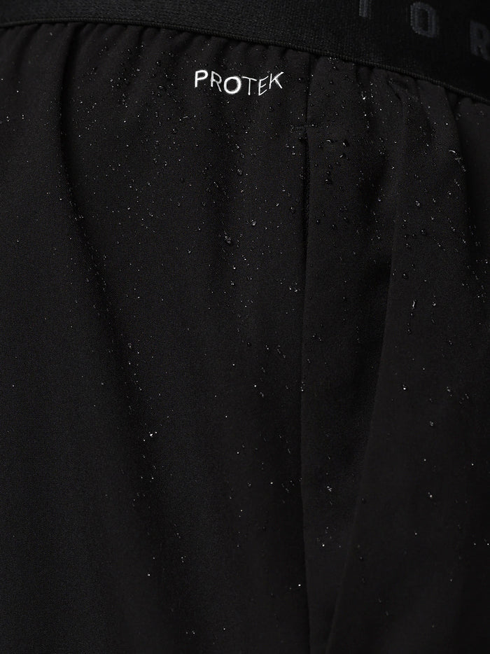Close-up of black Adapt Training Short fabric with water droplets and ProTek branding on the waistband