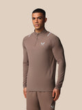 Male model wearing taupe Castore Apex training top with quarter zip and reflective shoulder accents