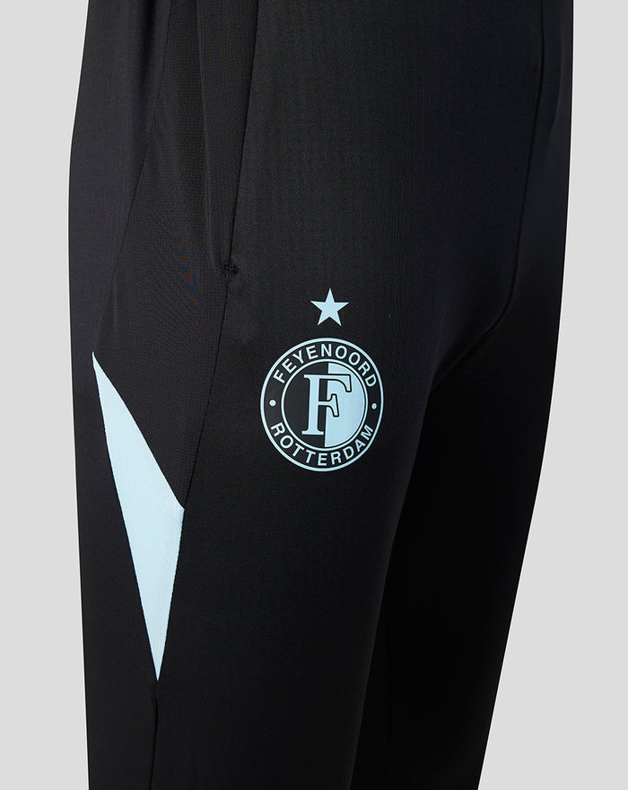 Detail van een zwarte trainingsbroek met Feyenoord badge op het bovenbeen en een lichtblauw zijaccent