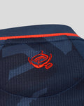 Close-up of navy Feyenoord women's third shirt showing orange piping along the seam and embroidered Castore logo on the fabric.