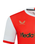 Close-up of Feyenoord 2025-2026 home shirt shows gold Castore emblem on red panel and MediaMarkt sponsor across the chest