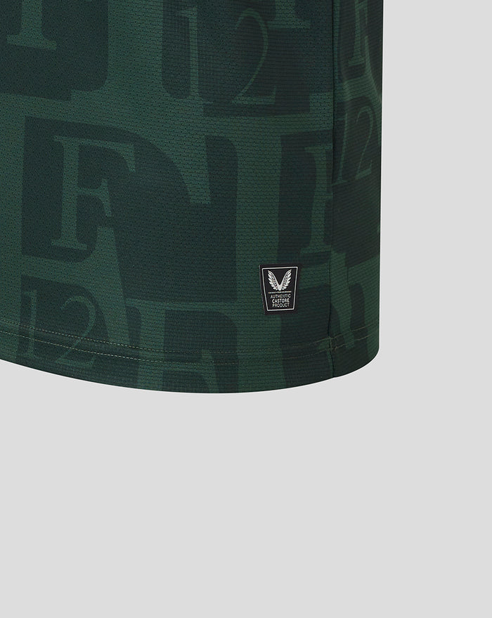 Close-up of dark green Twaalfde shirt fabric with a small black Castore authenticity badge at the hem.