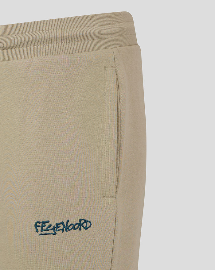 Close up of teal Feyenoord logo embroidery on the thigh of taupe joggers.